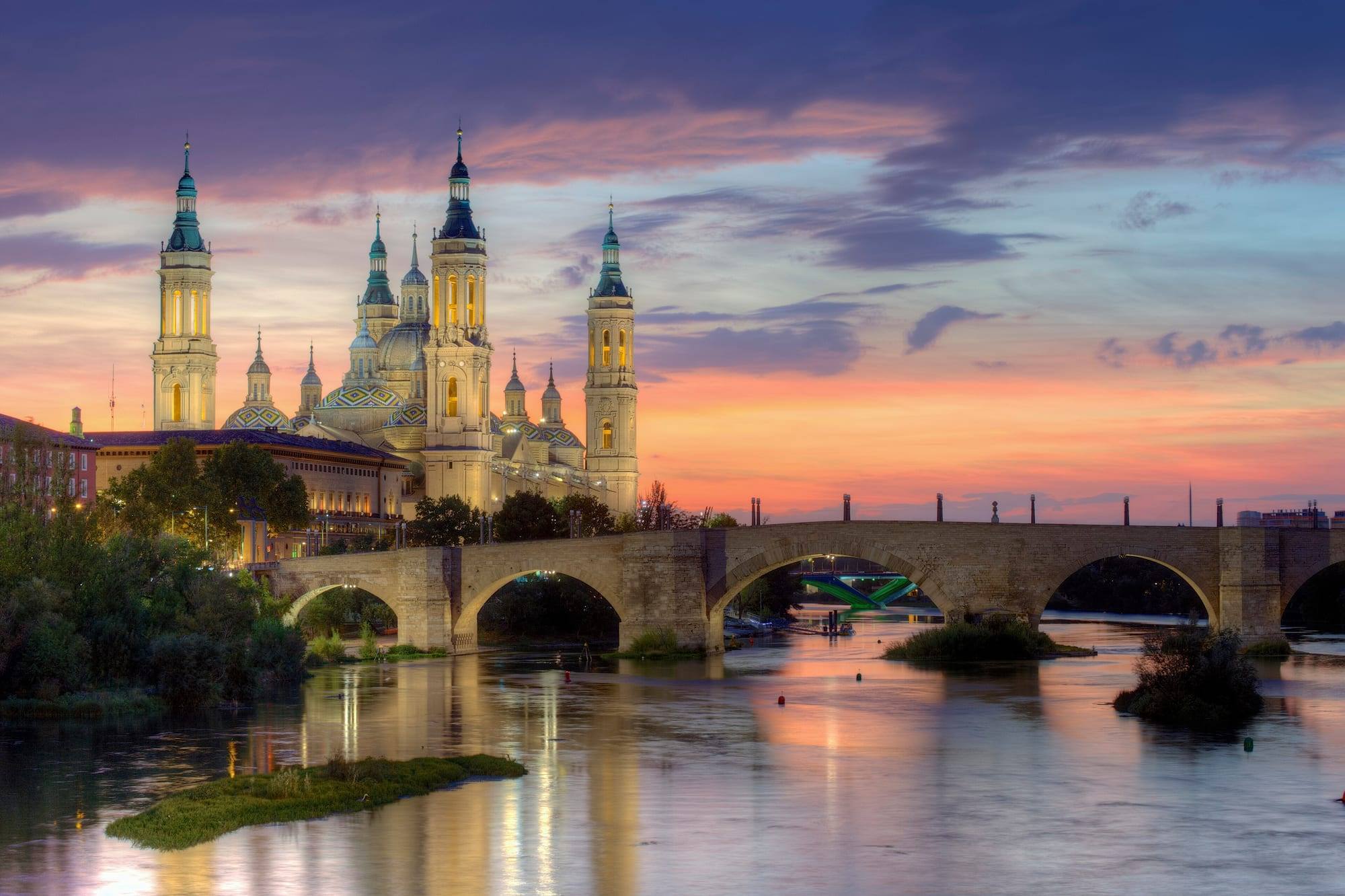 The Basílica del Pilar with its domes and four towers and the stone Puente de Piedra over the Ebro river at sunset, Zaragoza