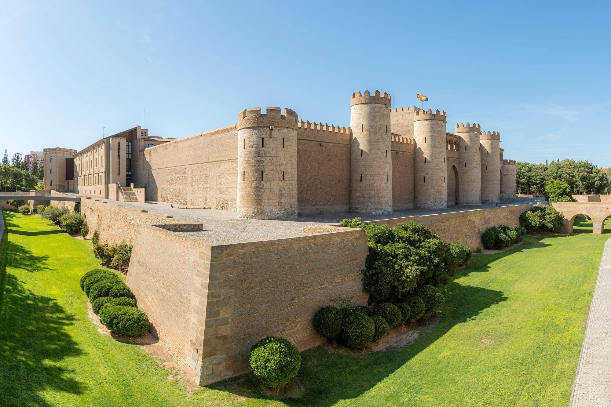 The Aljafería palace in Zaragoza: long brick walls and round towers above a landscaped grassy moat